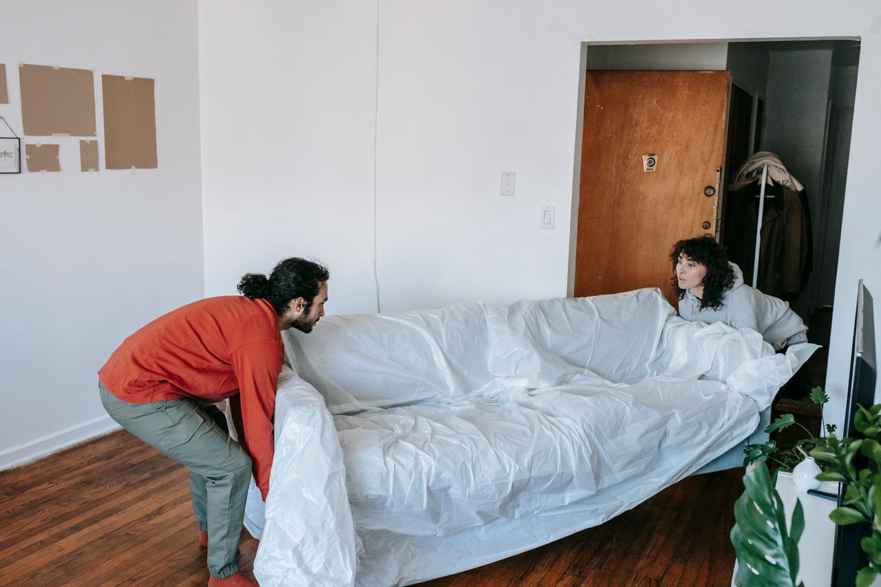 A couple working together to carry a couch as they move into a new apartment.